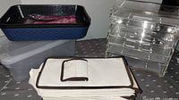 Photo shows multiple storage items including an acrylic jewelry box missing one drawer, black and blue plastic basket, translucent plastic basket, collapsible beige fabric basket, and beige tote with lid.