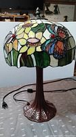 Full view of the Tiffany style lamp showing stained glass shade with butterfly and flower motif and bronze metal base.