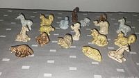 Photo of 18 Wade Whimsies vintage miniature animal figurines arranged on grey cloth, showing various animal types and coloration including beige, brown, white, and grey.