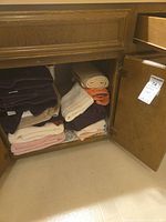 Photo showing a cabinet with multiple folded towels in varying colors including purple, beige, cream, orange, and pink, some stacked and some rolled.