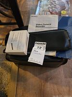 Photo shows two Sony video camera recorder manuals stacked on top of a zipped black carrying case. The note with MaxSold tags is present.