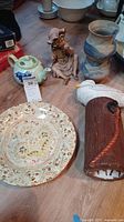 Lot of four ceramic items on wooden floor: green teapot, pottery vase, decorative plate, bird figurine on base