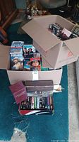 Boxes containing assorted DVDs and VHS tapes with visible titles including Pearl Harbor and Titanic.