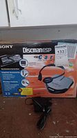 Box showing Sony Discman ESP text and images of included accessories like headphones and car cassette adapter. Maxsold lot sticker visible.