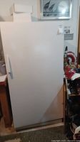 Front view of a white upright freezer, plain door with handle on left side from front.