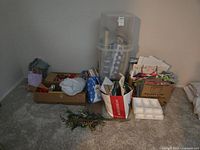 Overall view of boxes and bags containing gift wrapping supplies including bags, paper, ribbons, bows, and holiday decor.