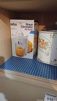 Braun Citromatic juicer box and ceramic crockpot on shelf with blue tile surface