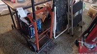 Photo showing the red dolly hand truck, black foldable table, and part of the white ladder and black ladder behind.