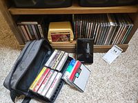 Photo showing cassette tapes, vintage radio, Sony Walkman with earbuds, and carrying case along with CDs on shelf