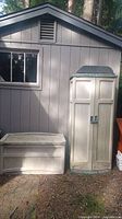 Outdoor location photo showing both a rectangular storage bench and a tall narrow storage shed side by side.