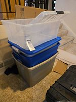 Stack of four plastic storage totes: one large gray tote at the bottom without a lid, two blue totes stacked with lids in the middle, and one clear tote with lid on top.