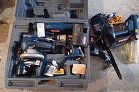 Overview of power tools inside gray plastic carrying case including drill, grinder, charger, others