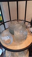 Photo showing stacked clear glass plates and bowls along with large crystal serving dish and etched oil decanter on a chair seat.