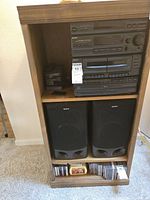 Full view of wooden media cabinet containing stereo system components, two speakers below, and CDs on bottom shelf.