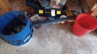 Stanley toolbox, blue collapsible tool bucket, red bucket, two long black rods, and hand tools on concrete floor
