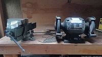Bench vice on left and bench grinder on right placed side by side on wooden surface.