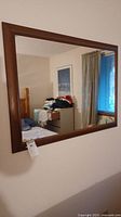 Rectangular framed wall mirror with wooden frame reflecting room interior.