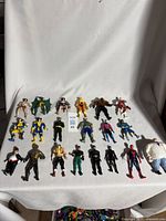 Full layout of approximately 20 1980s-1990s Marvel and DC Comics action figures on white fabric background, showing varied characters.