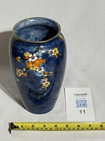 Full view of the vase showing blue mottled glaze and floral decoration with a measuring tape for scale.