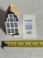 Front view of Delftware canal house figurine next to a measurement tape showing height approximately 4 inches.
