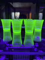 Four green uranium glass shot glasses glowing bright yellow-green under UV light, reflected on a glossy surface.