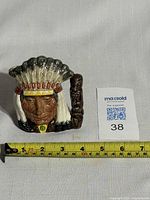 Front view showing the detailed face of the Native American chief with feathered headdress and carved staff handle.