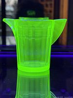 Bright green uranium glass creamer under UV light showing fluorescence.