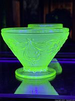 Uranium glass sherbet sugar bowl glowing green under UV light, showing its unique fluorescent property.