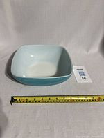 Square turquoise Pyrex bowl placed next to measuring tape showing width about 8 inches