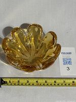 Top and angled top views of a gold-colored art glass bowl with scalloped edges and approximately 7-inch diameter, showing smooth glossy finish and heavy base