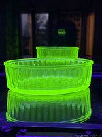 Oval uranium glass dish glowing bright green under UV light showing characteristic fluorescence.