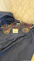 Three Pyrex glass liquid measuring cups in small, medium, and large sizes placed on a fabric background