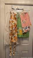 Four vintage aprons hung on a door, showing variety in color and pattern