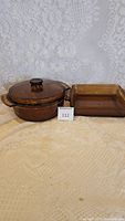Round amber glass pot with lid and one 8x8 square baking pan side by side on lace background.