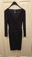Full view of the black long sleeve dress hanging on a hanger against a door, showing overall shape and length.