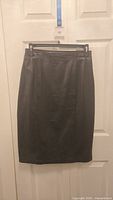 Full front view of black leather skirt hanging on black hanger with measuring tape behind showing approximate length.
