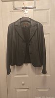 Full front view of the black leather jacket hanging on a hanger showing style, buttons, and collar.