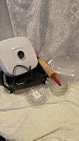 Electric frying pan with white lid, vintage rolling pin, white casserole with glass lid, three clear glass bowls, and four cut glass side plates arranged together.