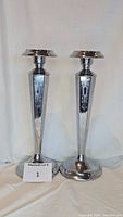 Pair of polished chromium candlesticks shown upright on white background, with lot number card