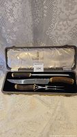 Full view of carving knife and fork set in original fitted case on lace fabric background