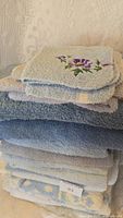 Photo showing folded stack of blue and light blue towels with floral embroidered towel on top