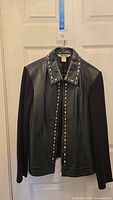 Front view of the black leather jacket with studded collar and sleeves made of different fabric material.