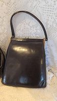 Vintage black leather handbag with metal frame and short handle shown on lace background