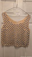 Front view of beige knit sleeveless top with blue and clear bead embellishment hung on a hanger