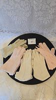 Four pairs of vintage ladies gloves in white, beige, and pink arranged on a black circular surface with a lot number card.