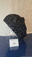 Side view of the black ruched fabric hat displayed on a clear stand with MaxSold lot number 18 sign.