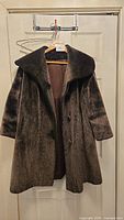 Full view of the deep brown fake fur coat hung on a door hanger showing the collar, sleeves, and button front.