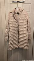Front full view of the cream padded women's coat on a hanger, showing the quilted design, long length, and zipper and snap closure.