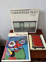 Three vintage art books on a wooden surface featuring Christopher Pratt, Karol Appel, and Paul Klee. Covers and condition visible to show wear and intact pages.