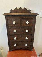 Front view showing five drawers with white porcelain knob handles and decorative top edge.